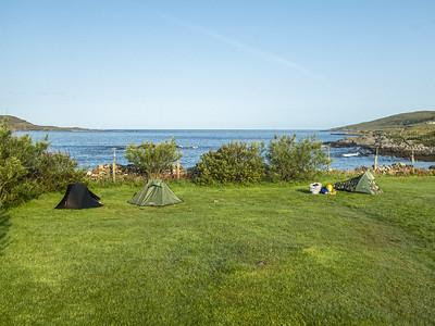 Three tents in grassy field under a clear sky with a sea bay in the background